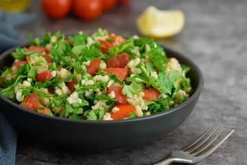 Tabbouleh salad with bulgur, parsley, spring onion and tomato in bowl on grey background. Side view