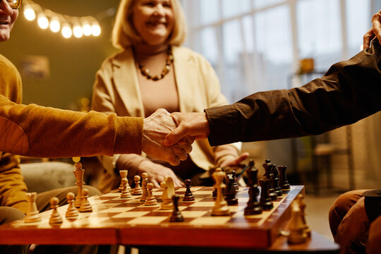 Two unrecognizable chess players shaking hands in the end of game while aged Caucasian woman smiling on background