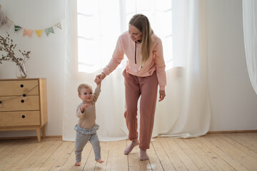 Young mother teaching to walk her cute little baby. Portrait of happy family at home. Care, first step concept  