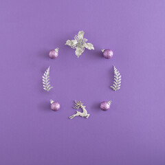 New year  flat lay with silver and pink decoration baubles, reindeer, flower and branches on violet background. Creative Christmas minimal copy space concept.