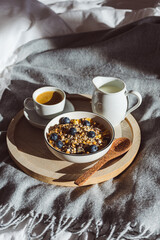 Frühstück mit einer Tasse Kaffee und Müsli mit Obst in einer Schüssel auf einer Bettedecke. Hygge, morgen.