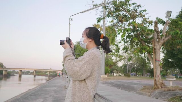 Asian woman standing and taking a picture of the river view in the evening Holding camera with park background in relaxing day