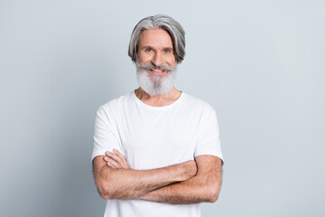 Photo of cheerful attractive man pensioner dressed white t-shirt smiling arms folded isolated grey...