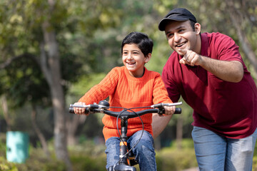 Cheerful father teaching son riding bicycle while admiring view at park.
