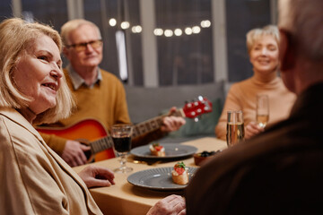 Over the shoulder view of old Caucasian woman tenderly looking at her husband sitting nearby while having dinner with friends