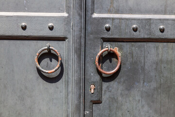 Close-up of the building's facade and an antique-style Wooden black door with round iron ring handles. Textured stone tiles and an old wooden door