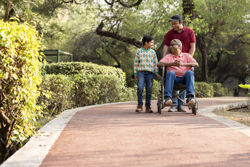 Man pushing old father on wheelchair while admiring view with son at park
