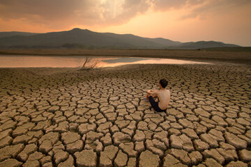 Young man sitting on dry cracked earth near drying river that impact by Drought.