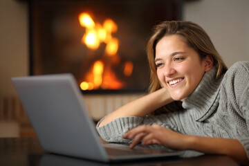 Happy woman using laptop at home near fireplace