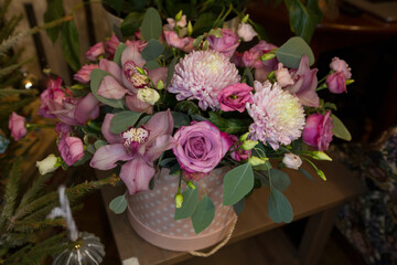 Obraz na płótnie Canvas flower bouquet arrangement in pink purple tones with roses, chrysanthemums, cymbidium orchids in a paper cylinder basket on a table 