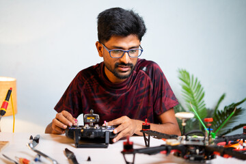 Young professional engineeer examining or testing drone configuration setting using remote control while repairning drone at shop - concept of uav or quad copter repair service and hobby.