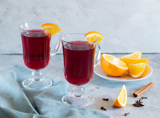 Two glasses of mulled wine, oranges, spices, light background, gray textiles