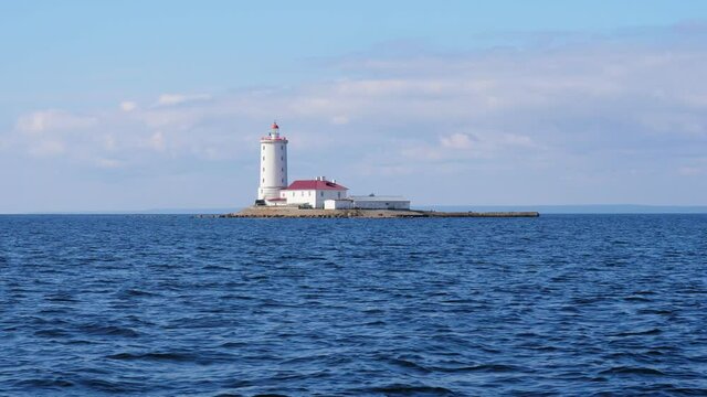 Tolbukhin lighthouse near Kronstadt island, view from boat in summer day. Historical buildings at artificial island. Inhabited place with only personnel (lighthouse keeper) living in two-storey home