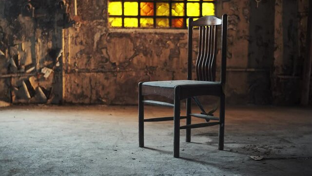 wooden old chair stands in middle of abandoned building or factory with yellow stained glass window, mid afternoon, yellow light falls on seat. concept of loneliness and post-apocalypse.