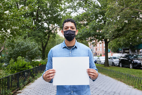 USA, New York, New York City, Portrait of man in face mask holding blank sign in city