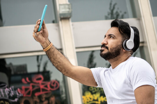 Latin man with beard, taking selfie. In the background walls with spray paint writings.