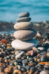 Fototapeta na wymiar Beautiful pyramid of pebbles on the seashore on a sunny day, copy the space. Concept of balance, harmony. Vertical photo