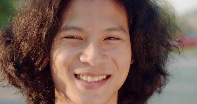 Smiling and laughing young Asian man with long hair in the evening sun.