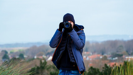 Fototapeta premium Young male adult taking a foto with professinal camera and bokeh background, wearing a blue jacket and blue hat
