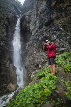 Russia , Karachay-Cherkessia, Arkhyz, Caucasus mountains, Hiker taking picture near waterfall