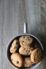 Ceramic bowl filled with chocolate chip cookies on wooden table. Flat lay.
