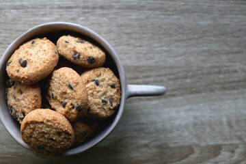 Ceramic bowl filled with chocolate chip cookies on wooden table. Flat lay.