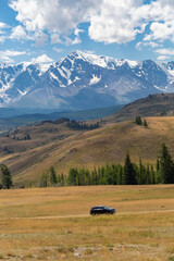 black car driving on dirt road in Kurai area with North Chuisky Ridge on background.