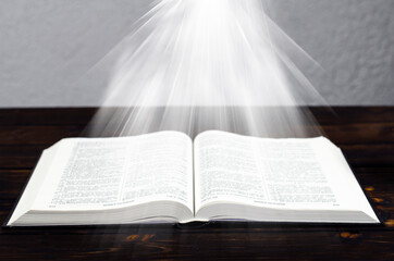 Open Bible, on a wooden table. Light from the book. Desktop.