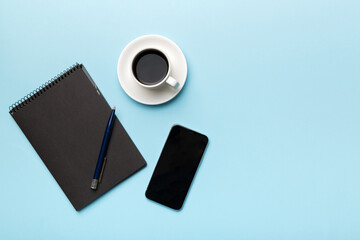 Modern office desk table with notebook, smartphone and other supplies with cup of coffee. Blank notebook page for you design. Top view, flat lay