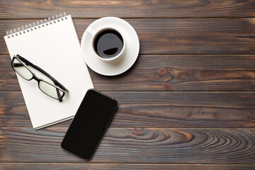 Modern office desk table with notebook, smartphone and other supplies with cup of coffee. Blank notebook page for you design. Top view, flat lay