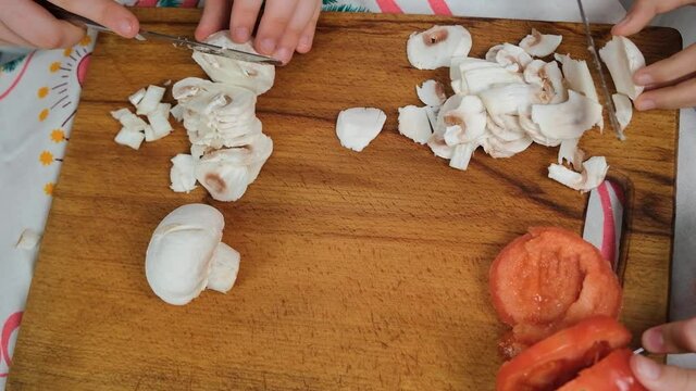 Children cooks pizza. Prepering ingredients for pizza. Children cut mushrooms and tomatoes on the board. Preparing tasty pizza together. At home, in kitchen. Mozzarella-mushroom pizza recipe, close up