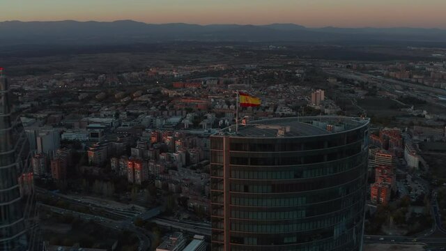 Aerial shot of tops of skyscrapers in CTBA business hub. Spanish flag on rooftop. City at dusk in background.