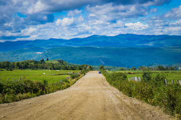 Fototapeta na wymiar View of an unpaved road in the Charlevoix countryside with view on the mountains in the background