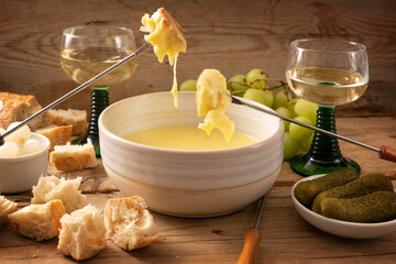 Swiss fondue from melted cheese with bread on long forks, pickles, grapes and wine on a rustic...