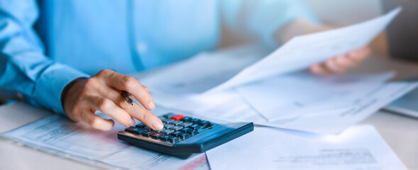 Woman using calculator with doing finance at home office. using a calculator to calculate the numbers, finance accounting concept.
