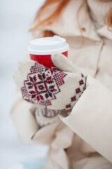 A girl in mittens holds a red disposable paper cup. Christmas mood.