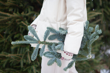 A girl in a beige jacket holds a spruce branch in her hand. Christmas mood.