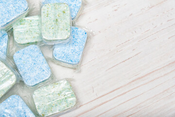 Green and blue dishwasher soap tablets in water-soluble packaging close up on the table with copy space