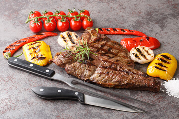 Grill T-bone beef steak with garlic, peppers and tomatoes close-up on a concrete gray background....