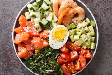 Keto diet portion for breakfast of salmon, shrimp, eggs and fresh vegetables close-up in a plate on a concrete table. horizontal top view from above