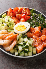 Keto salad of salmon, shrimp, eggs and fresh vegetables close-up in a plate on a concrete table. vertical