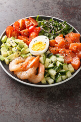 Delicious healthy salad of salmon, shrimp, eggs, avocado, cucumber and tomatoes close-up in a plate on the table. vertical