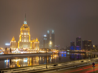 Fototapeta premium Illuminated high-rise stalinist building near river at winter night in Moscow, Russia. Historic name is Hotel Ukraine.