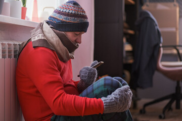 Man feeling cold at home having problems with home heating sitting with phone.