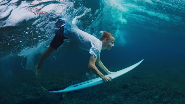 Teen boy dives underwater with surf board and confidently passes the wave