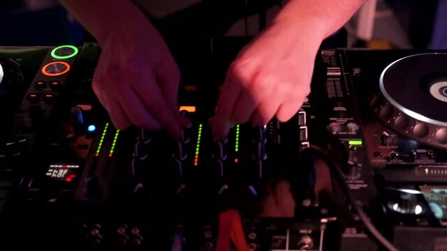 Tracking shot of a Man DJ playing with mixer and digital turntables. CDJ turntables with wires, button and sliders being played by electronic music Disc Jockey at nightclub. High quality 4k footage