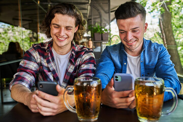 Two friends using mobile phone and drinking beer in pub.