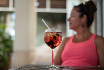 A selective focus shot of a young lady enjoying being sat outside with a nice glass of pink gin and tonic ready to be drunk - obrazy, fototapety, plakaty
