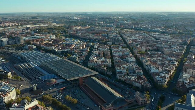 Forwards fly above urban neighbourhood. Large buildings of Atocha train station and traffic in streets around.