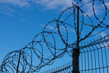 Barbed wire fence on background with blue sky and white clouds. Concept of freedom and prison...